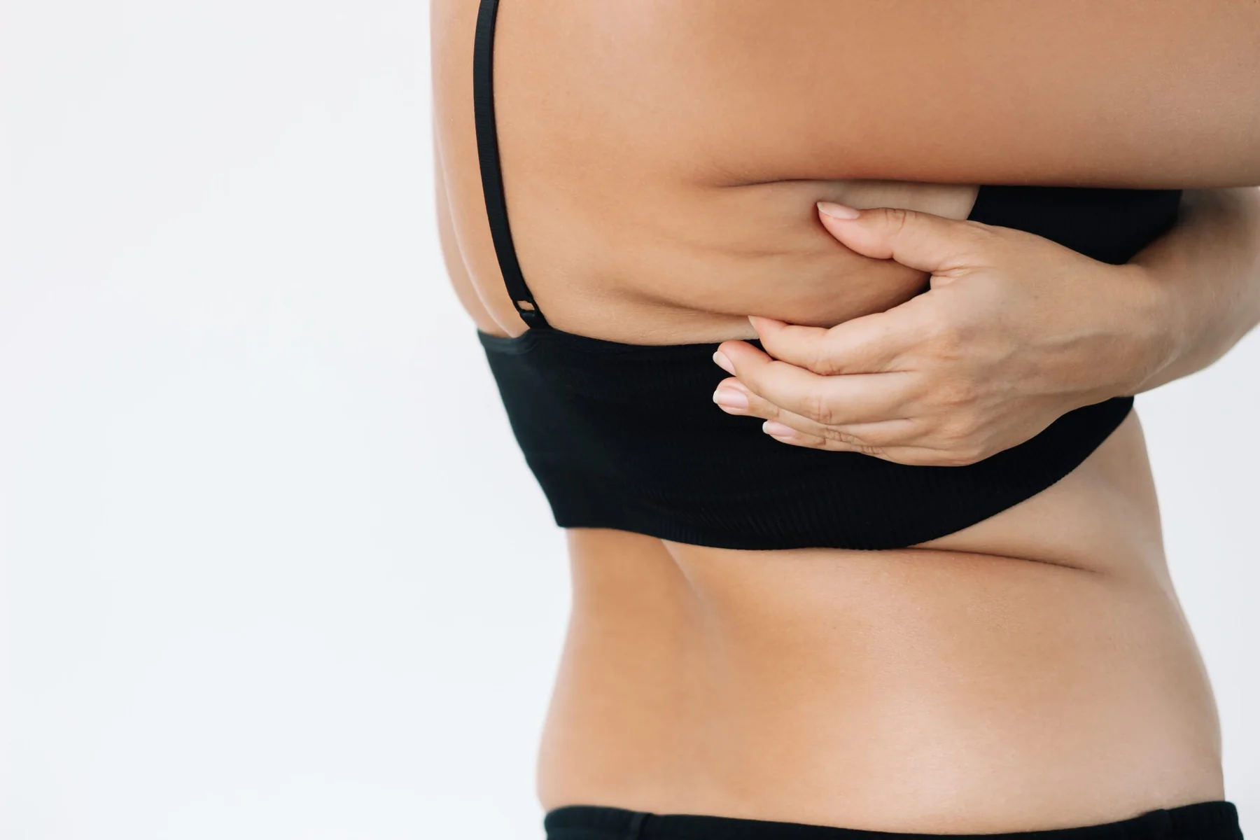 Woman grabbing skin with excess fat on her back under the arm above the bra.