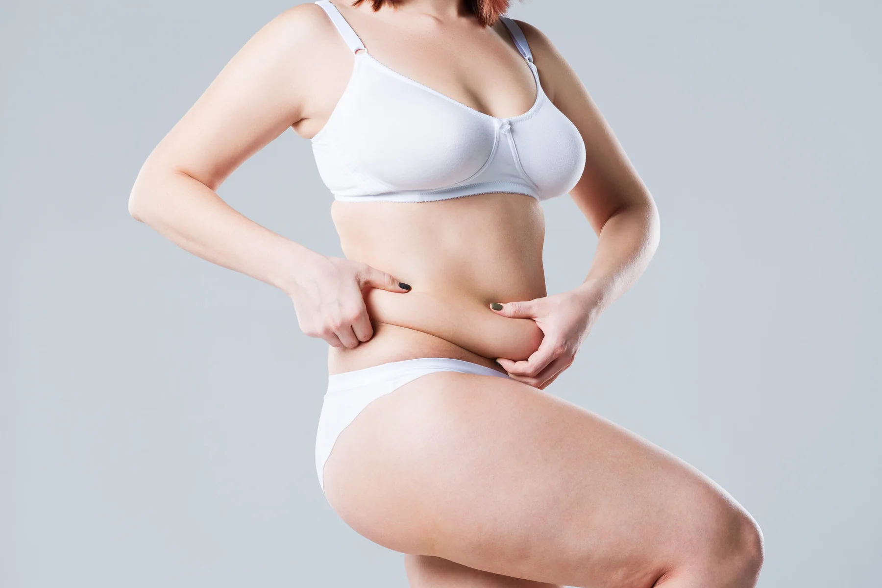 Woman turned to the side holding excess stomach fat with one leg bent.