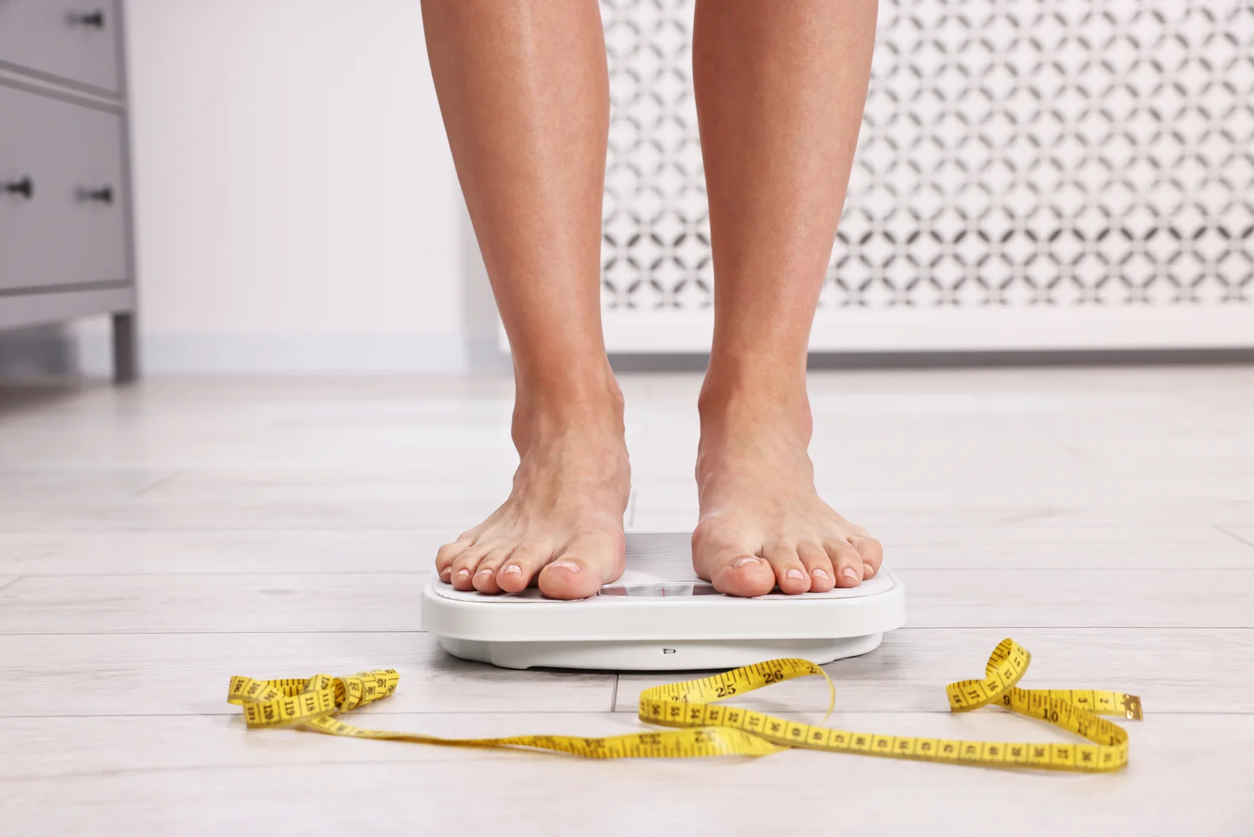 Woman stepping on a scale with a tape measure in front of her.